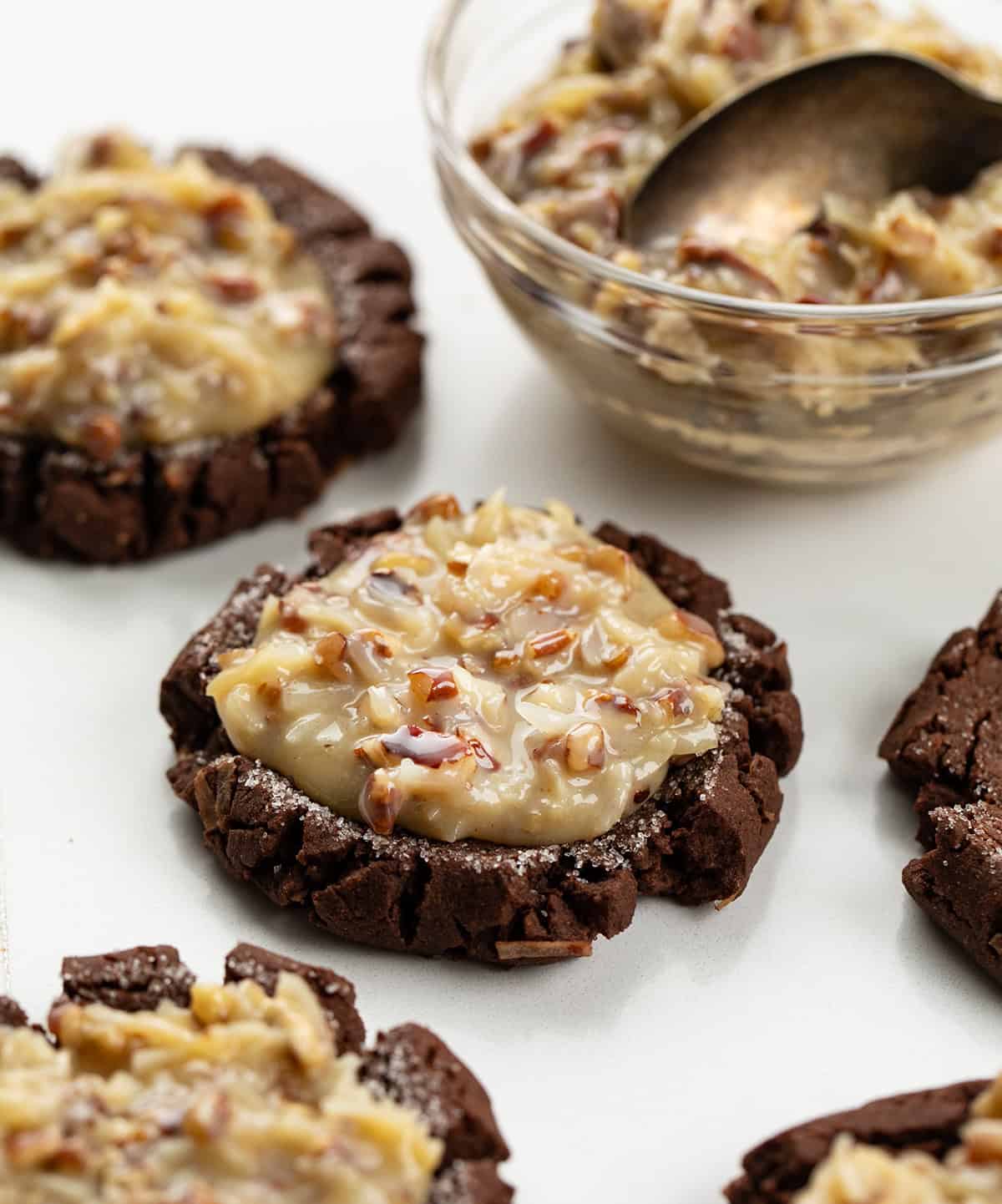 German Chocolate Cookies on a white table with german chocolate frosting in a bowl.