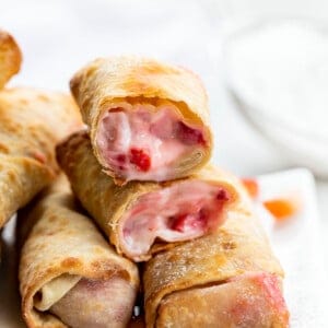Strawberry Cheesecake Egg Rolls Stacked on a White Plate and Broken in Half Showing the Inside