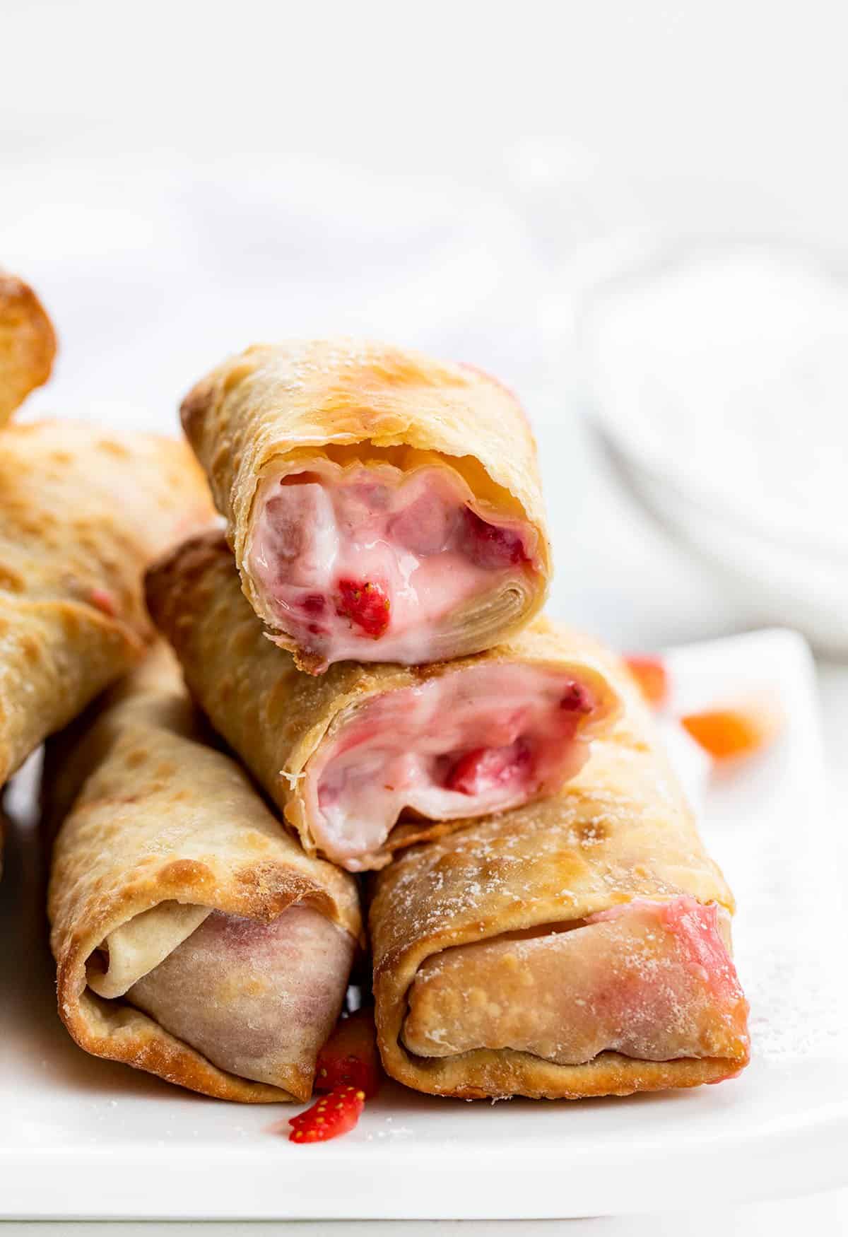 Strawberry Cheesecake Egg Rolls Stacked on a White Plate and Broken in Half Showing the Inside