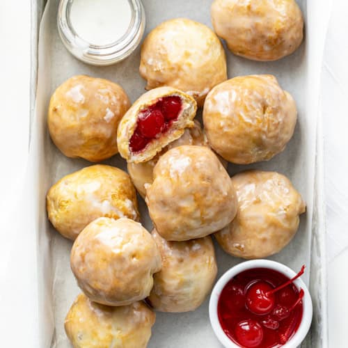 Cherry Pie Bombs in a Pan with Parchment, Glaze, and Cherries as well as one Cherry bomb cut in Half