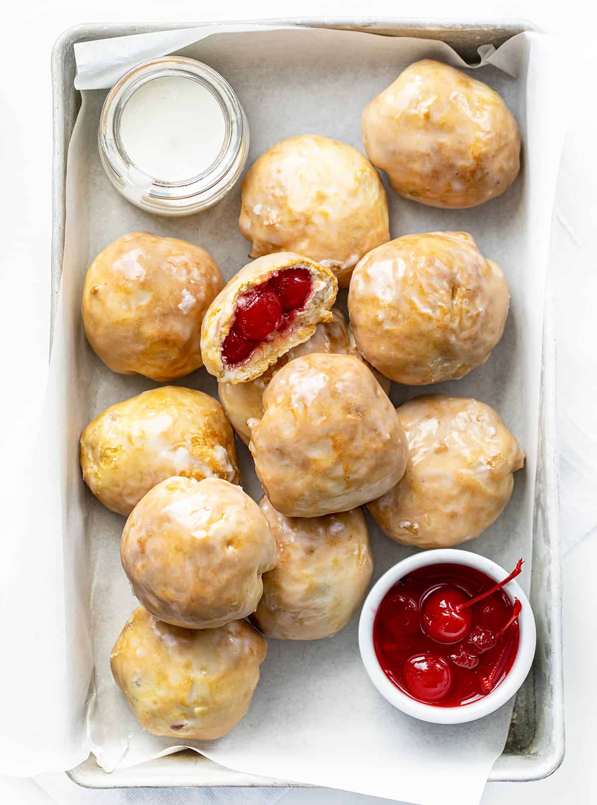 Cherry Pie Bombs in a Pan with Parchment, Glaze, and Cherries as well as one Cherry bomb cut in Half