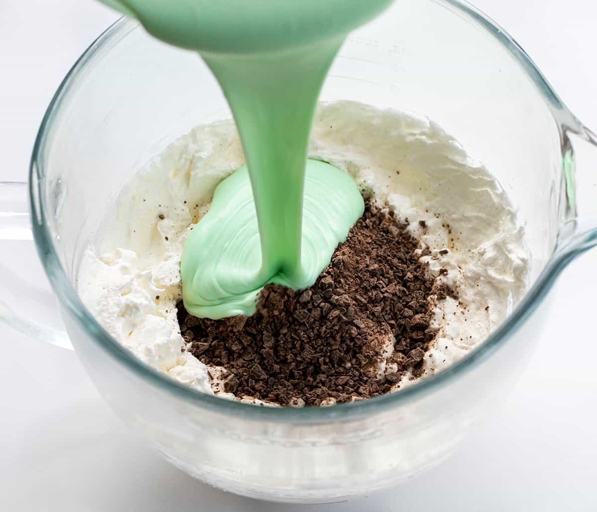 Adding sweetened condensed milk and chopped chocolate to whipped cream to make No-Churn Mint Chocolate Chip Ice Cream 