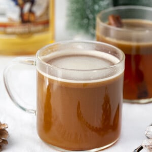 Glass of Hot Buttered Rum on Counter wtih Rum and Christmas Decorations.