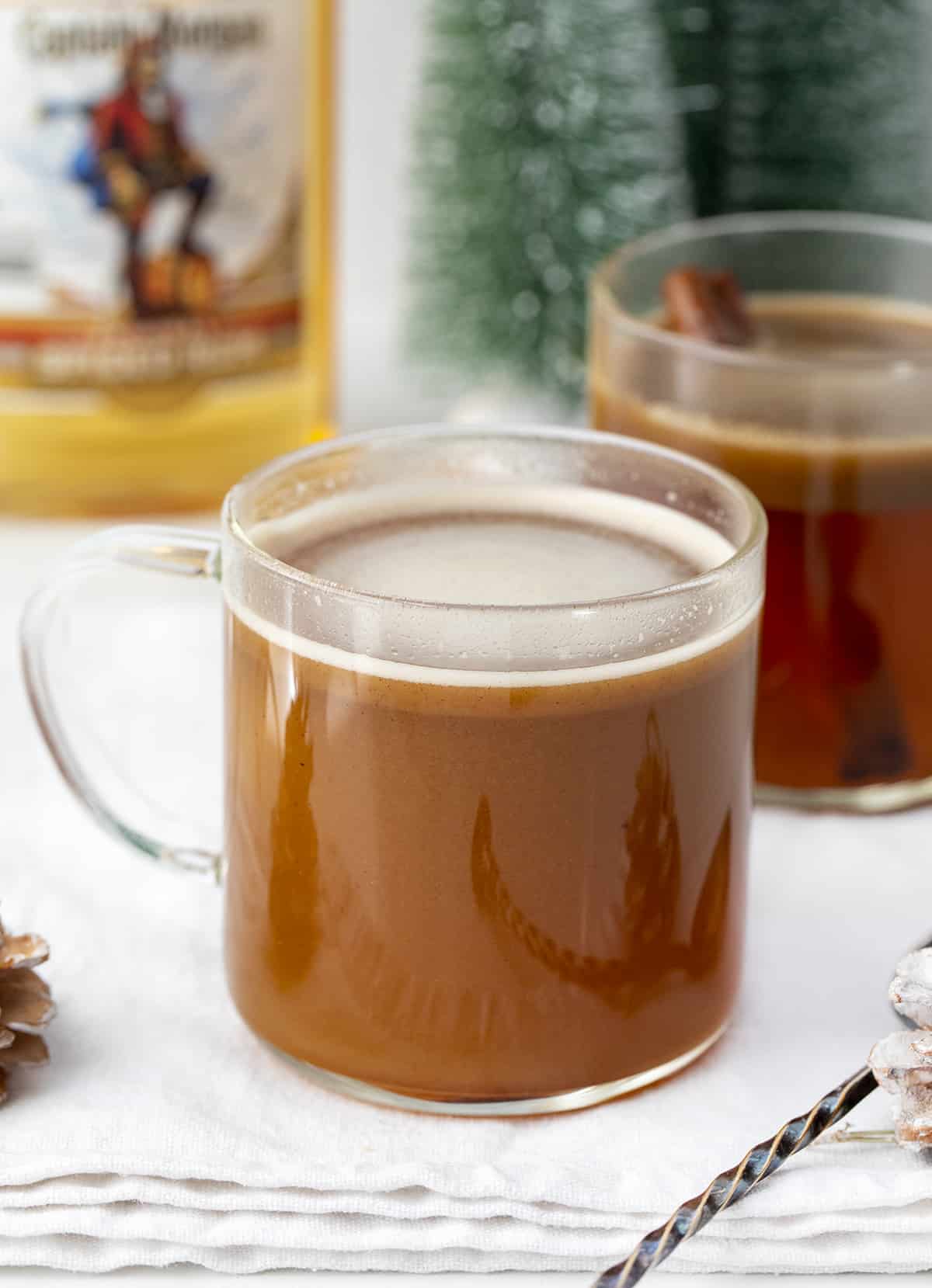 Glass of Hot Buttered Rum on Counter wtih Rum and Christmas Decorations.