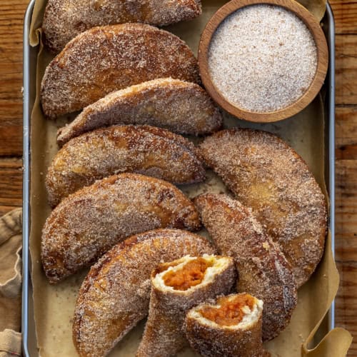 Pan of Pumpkin Hand Pies with One Broken in Half Showing Inside. Pumpkin Hand Pies, Pumpkin Bombs, Pumpkin Desserts, Pumpkin Snacks, Pumpkin Spice, Pumpkin Crisps, Fried Pumpkin Pies, Individual Pumpkin Pies, Cinnamon Sugar Pumpkin Pies, fall recipes, Thanksgiving Recipes, Christmas Recipes, Thanksgiving Desserts, i am baker, iambaker