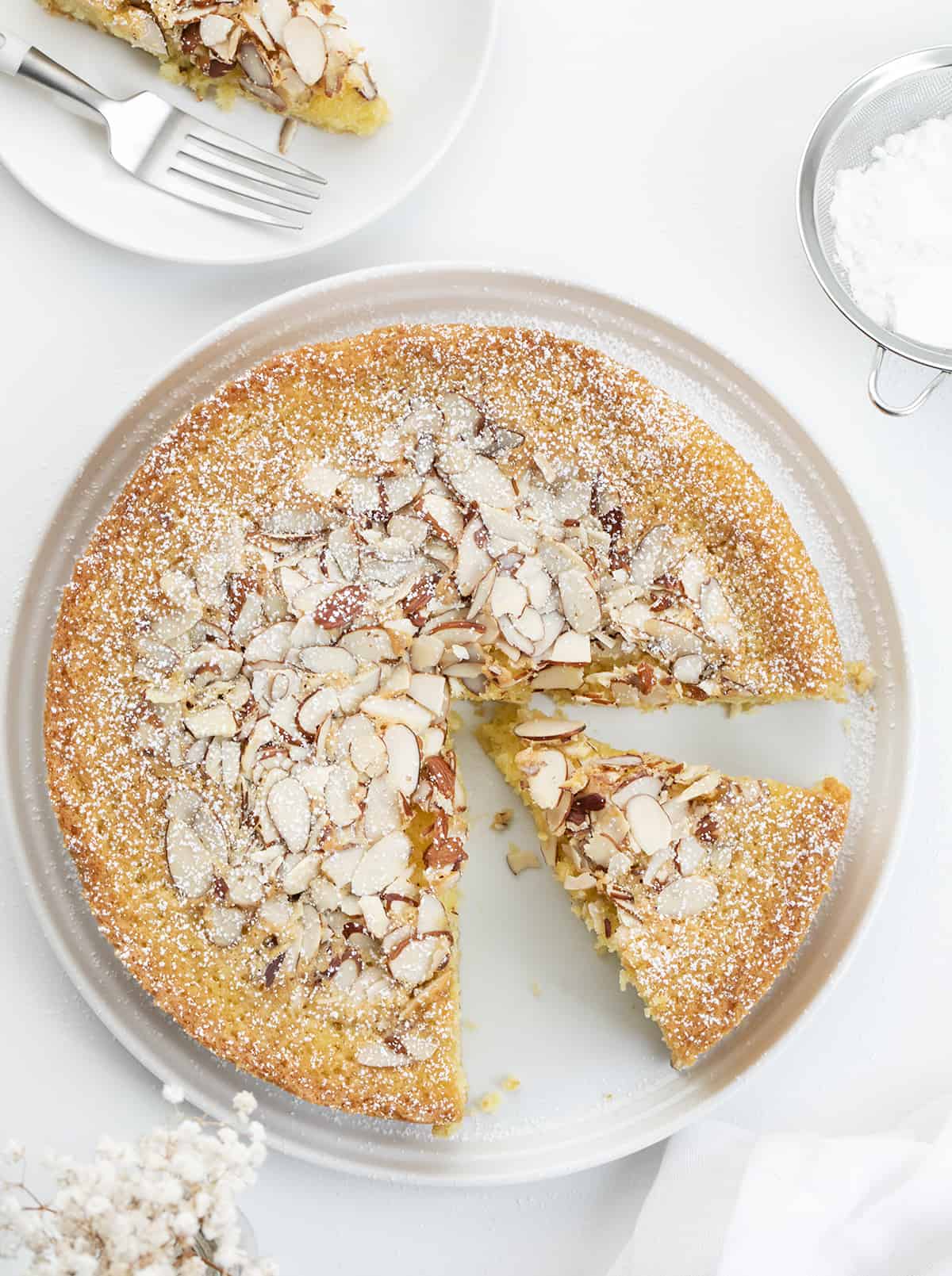 Almond Cake on a White Surface with Plates and Confectioners Sugar and a Slice Removed. Almond Cake, French Almond Cake, Moist Almond Cake, How to Make Almond Cake, Almond Cake Recipes, Easy Almond Cake Recipes, Baking, Dessert, Holiday Baking, Christmas Cake, Thanksgiving Cake, i am baker, iambaker