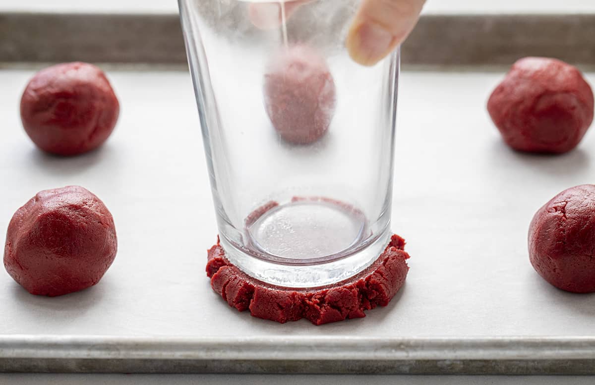 Glass Pressing Down a Ball of Red Velvet Cookie Dough to Make Red Velvet Cookies. Dessert, Cookies, Baking, Christmas Cookies, Holiday Baking, Cookie Exchange, Red Velvet Recipes, Red Velvet Cookies, Cream Cheese Frosting, Frosted Sugar Cookies, i am baker, iambaker