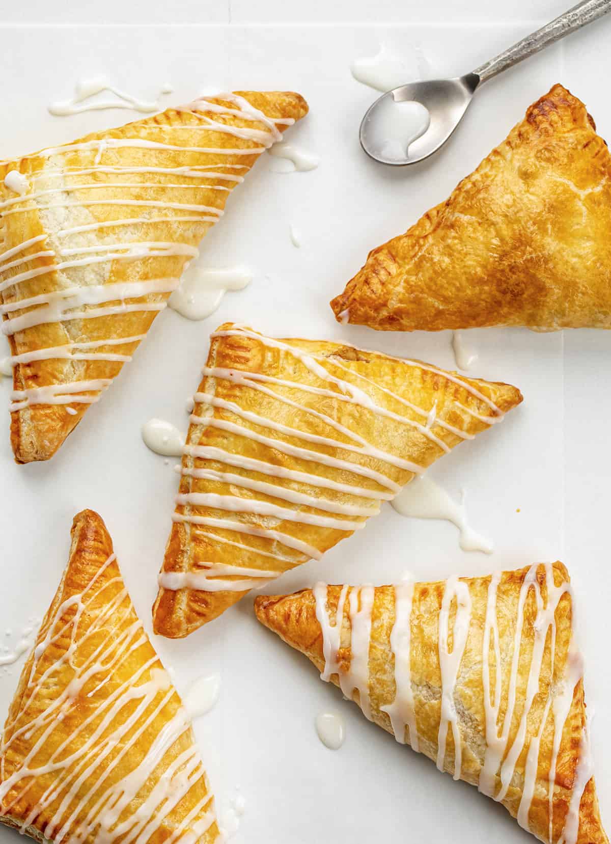 Apple Turnovers on a Counter with Glaze Drizzled Over Top and a Spoon.