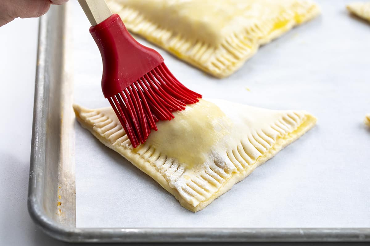 Brushing Egg Wash over unbaked Apple Turnovers.