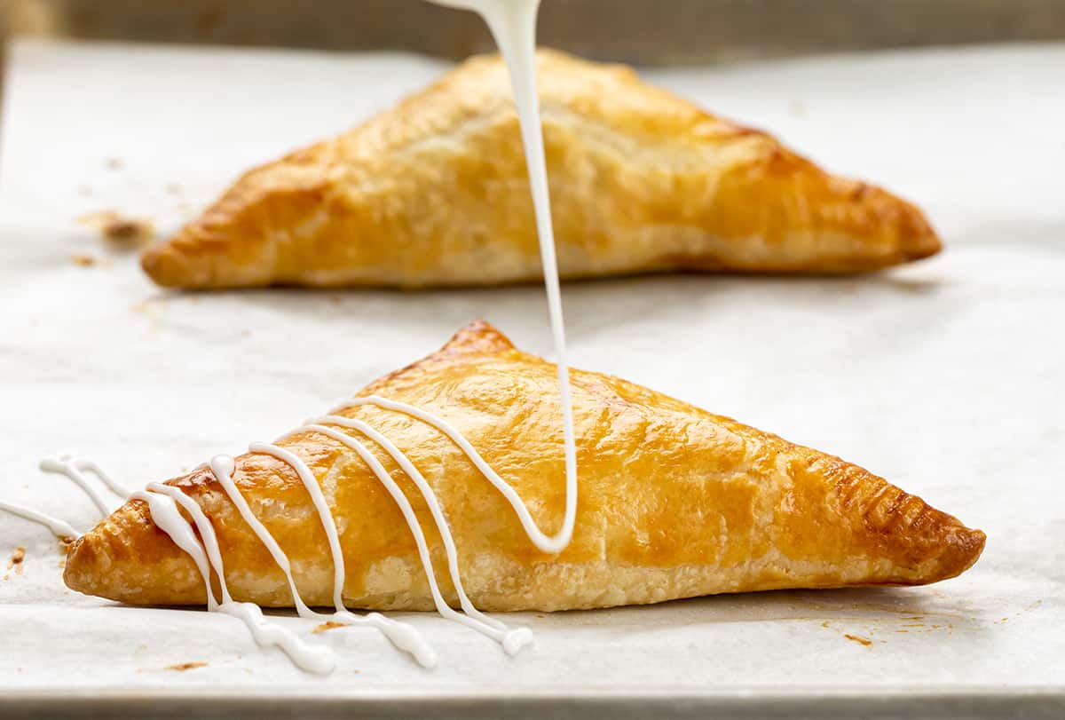 Drizzling Glaze Over Baked Apple Turnovers.