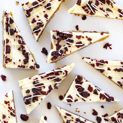 Triangles of Cranberry Bliss Bars Covered in Cream Cheese and Cranberries and Drizzled in White Chocolate.