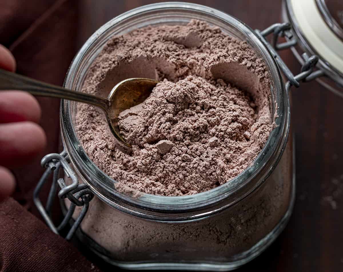 Spoon in a jar of homemade hot cocoa mix on a cutting board. 