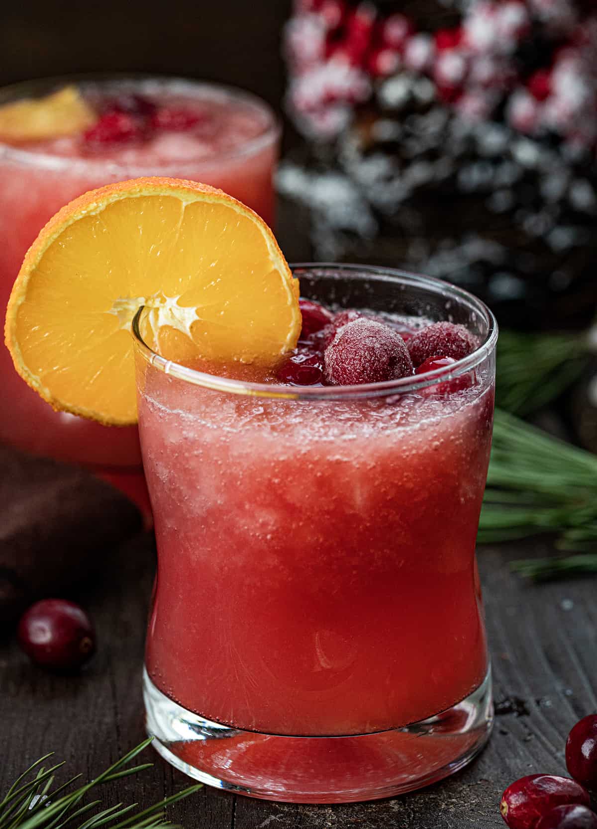 Glass of Christmas Slush with an Orange Garnish and Sugared Cranberries.