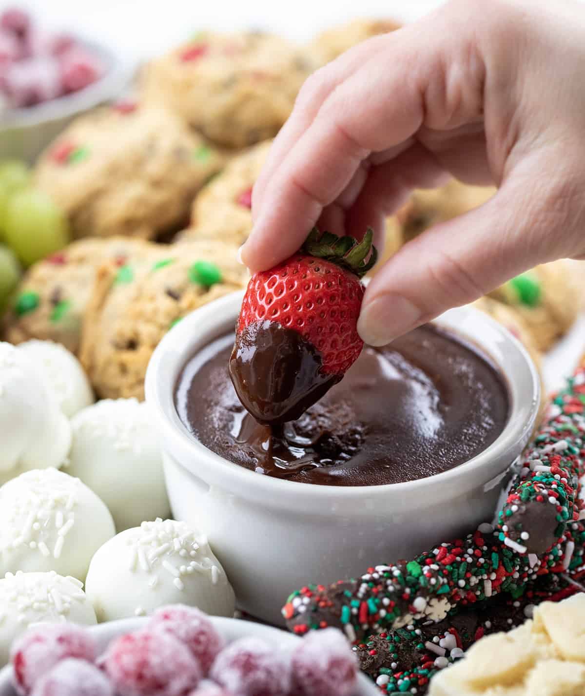 Dipping a Strawberry into Chocolate Ganache on a Christmas Dessert Charcuterie Board.