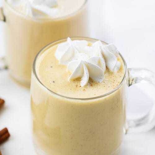 Glass mugs filled with eggnog and topped with whipped cream.