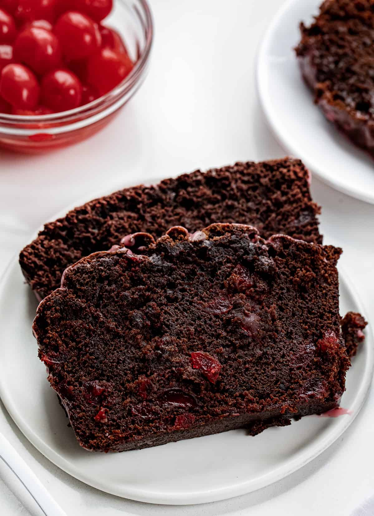 Close up of Cherry Brownie Bread Slices on a Plate with Cherries in the Background.