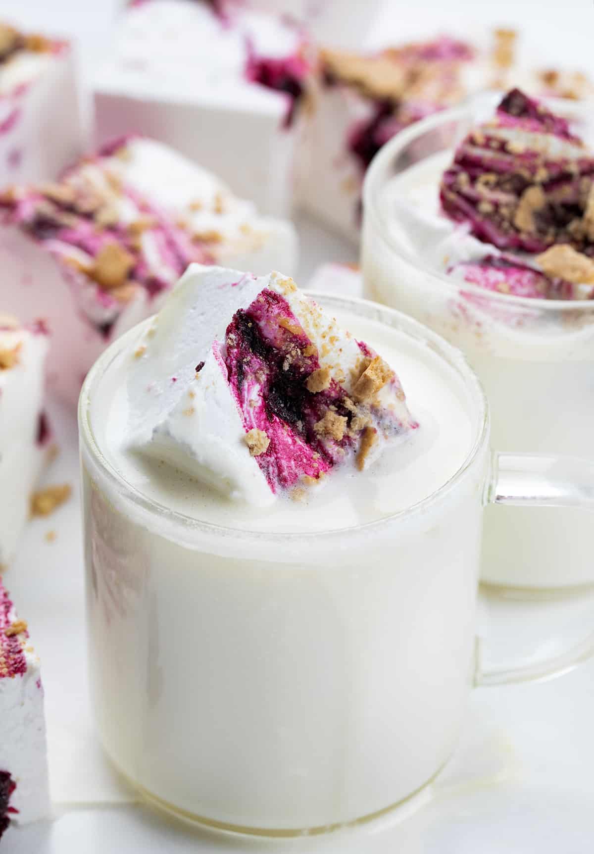 Pieces of Gourmet Blueberry Marshmallows On a White Surface and Cut into Squares. Next to Cups of White Chocolate Hot Cocoa.