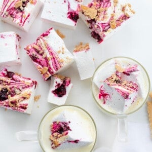 Pieces of Gourmet Blueberry Marshmallows On a White Surface and Cut into Squares. Next to Cups of White Chocolate Hot Cocoa.