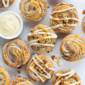 Carrot Cake Cruffins on a White Counter with Some Having Cream Cheese Drizzled Over Top and Some Plain.