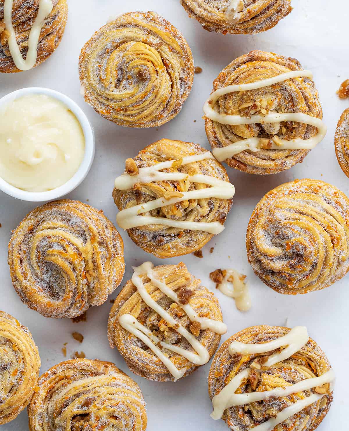 Carrot Cake Cruffins on a White Counter with Some Having Cream Cheese Drizzled Over Top and Some Plain.