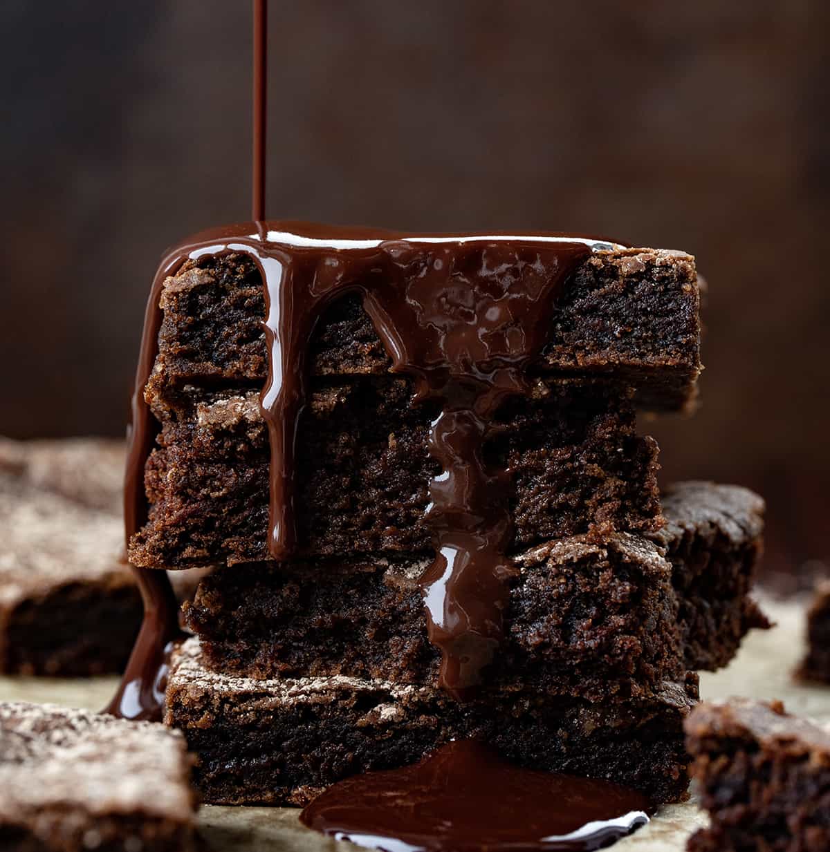 Chocolate Brownies Stacked on Top of Each other with Ganache Being drizzled on It.