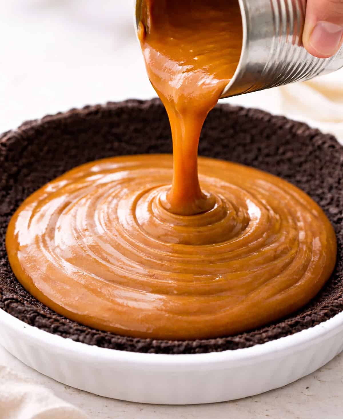 Pouring Dulce de Leche into a pie with oreo pie crust.