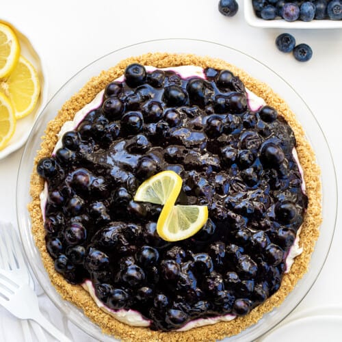 Looking Down on a Blueberry Lemon Cream Pie on a White Counter Surrounded by Blueberries and Lemons and White Forks.