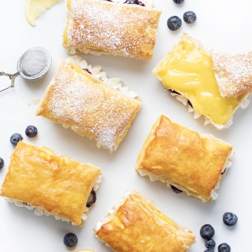 Blueberry Lemon Napoleons Layed Out on a Counter with One Showing the Lemon Curd Inside and Blueberries Scattered Around.