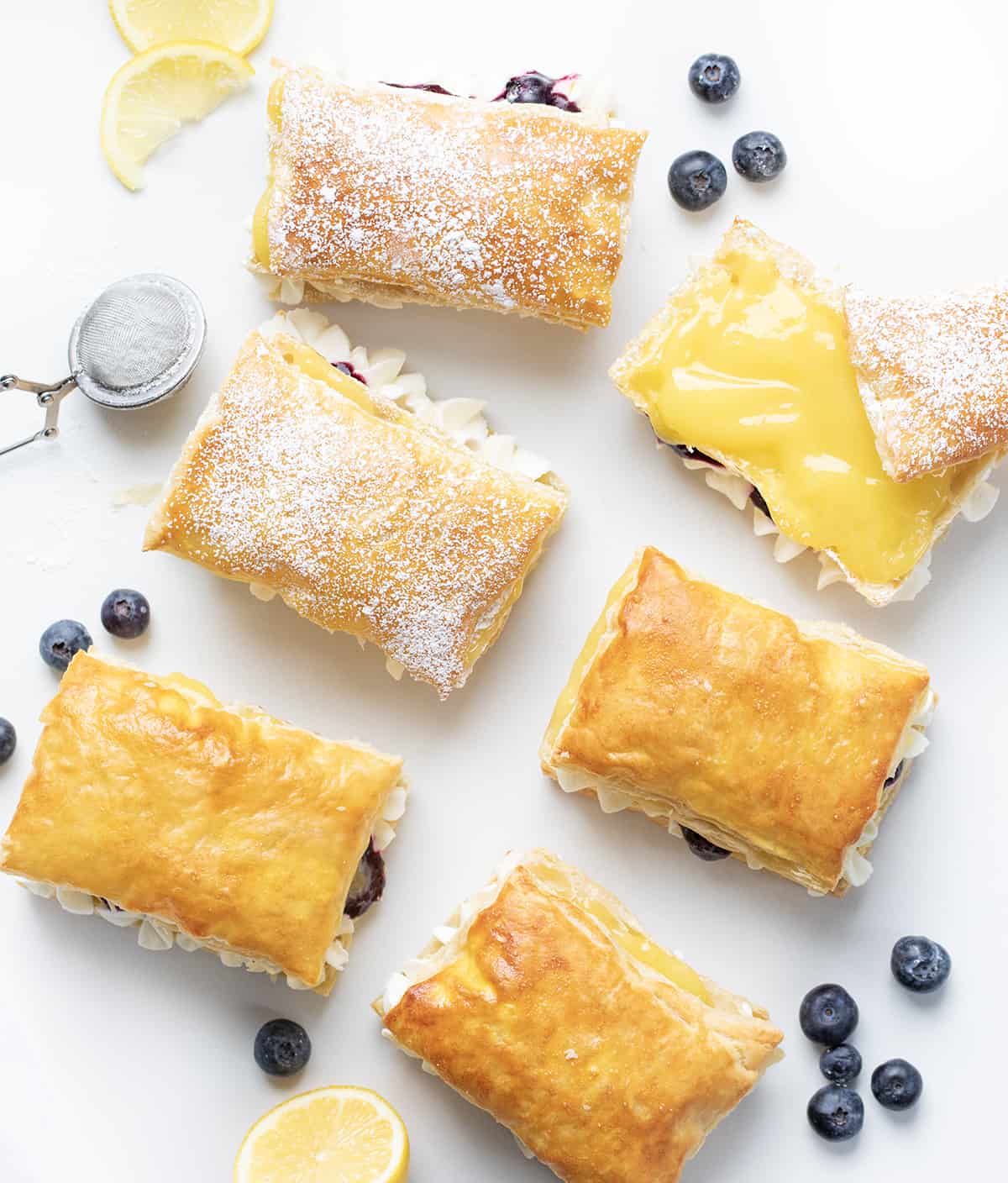 Blueberry Lemon Napoleons Layed Out on a Counter with One Showing the Lemon Curd Inside and Blueberries Scattered Around.