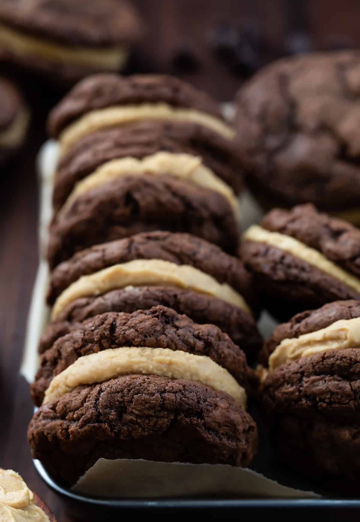Rows of Chocolate Peanut Butter Sandwich Cookies in a Dish on a Dark Cutting Board.