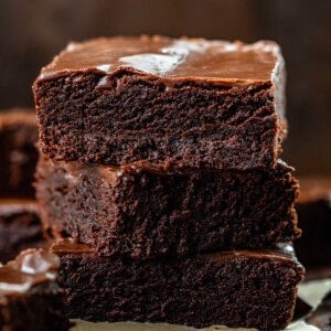 Three Double Fudge Brownies Stacked on Top of Each Other on a Dark Cutting Board.