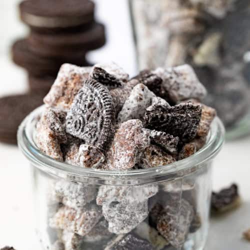 Jar of Cookies and Cream Puppy Chow on a White Counter and Close Showing the Oreos and Chocolate Covered Chex Cereal.