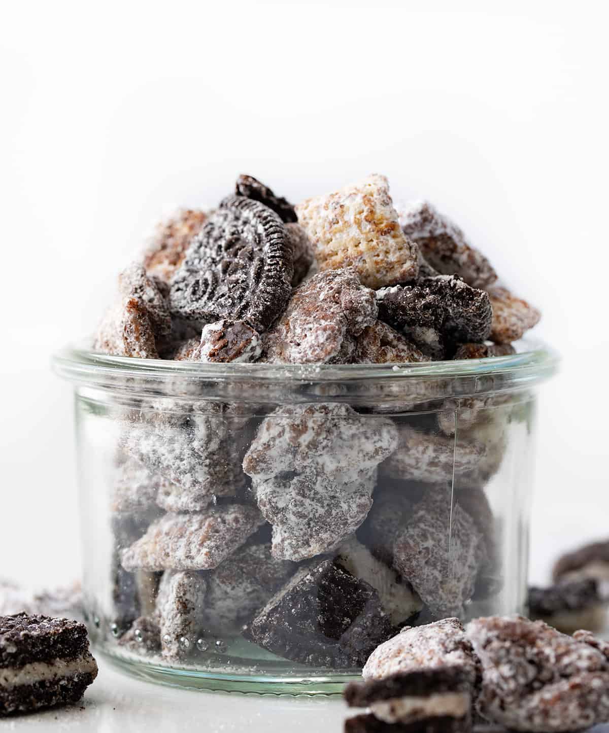 Jar of Cookies and Cream Puppy Chow on a White Counter and Close Showing the Oreos and Chocolate Covered Chex Cereal. 