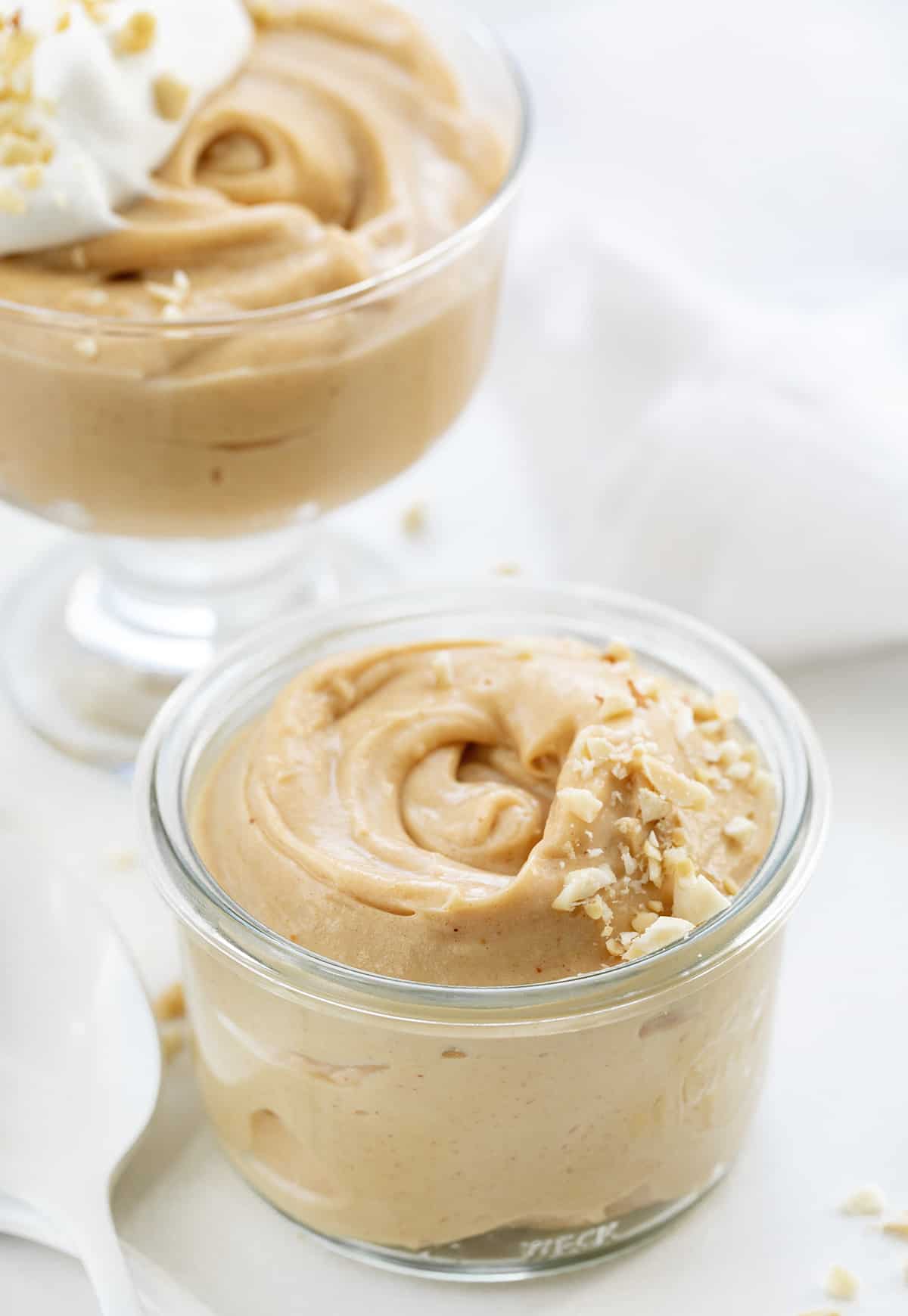 Two dishes of Peanut Butter Mousse With Chopped Peanuts Sprinkled on Top on a White Counter.