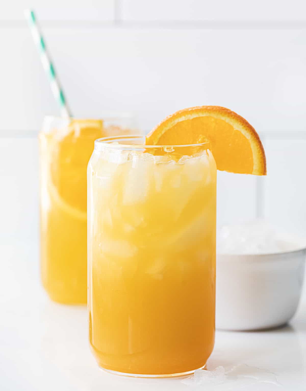 Glasses of Yellow Hammer Slammer with an Orange Garnish on a White Counter.