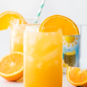 Glasses of Yellow Hammer Slammer with an Orange Garnish on a White Counter.