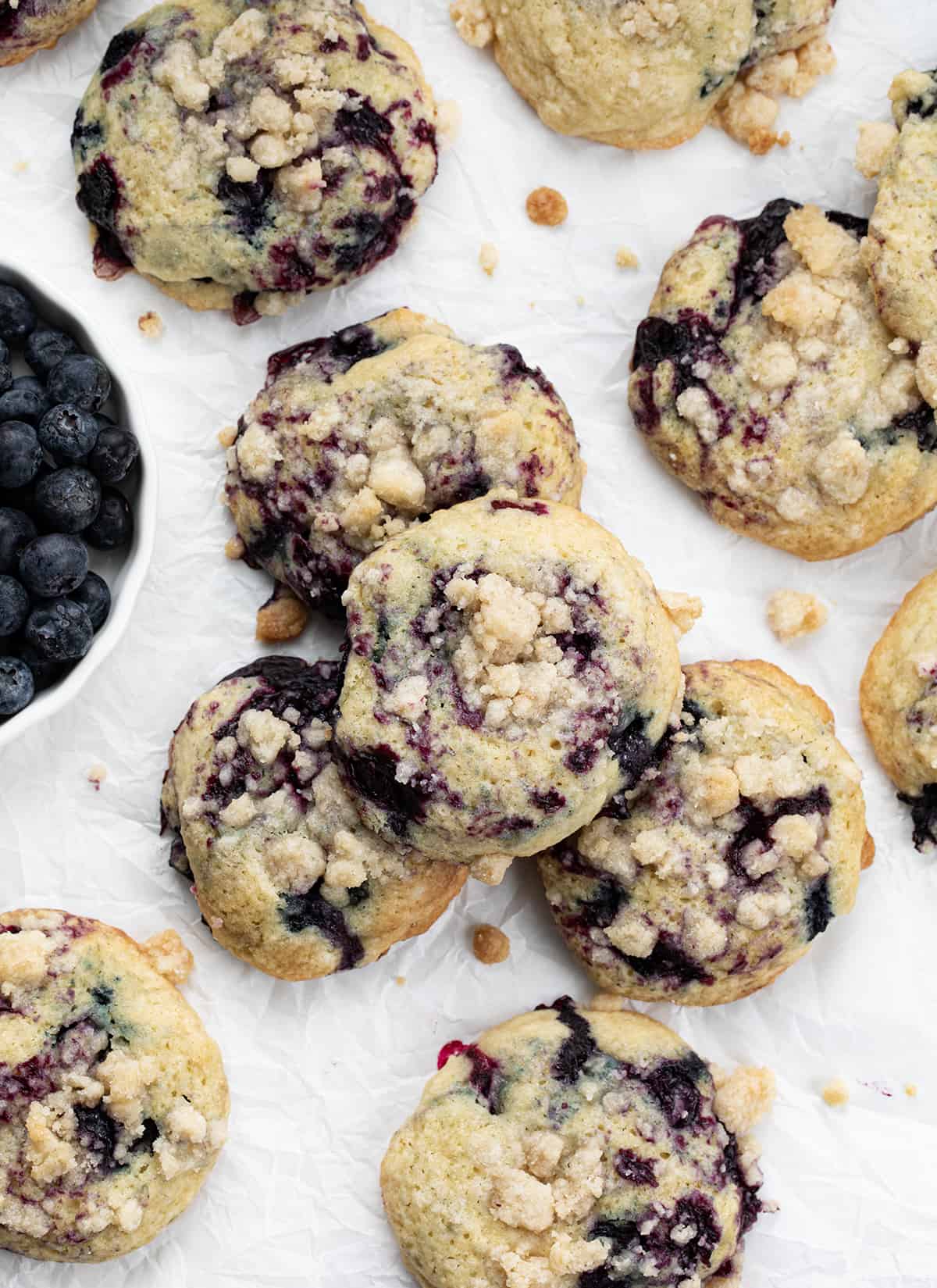Blueberry Crumble Cake Cookies on White Parchment Next to Fresh Blueberries.