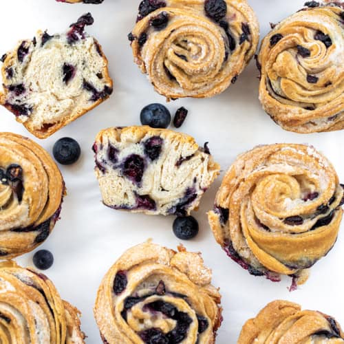 Blueberry Cruffins on a w White Counter with Most Whole and One Cut in Half.