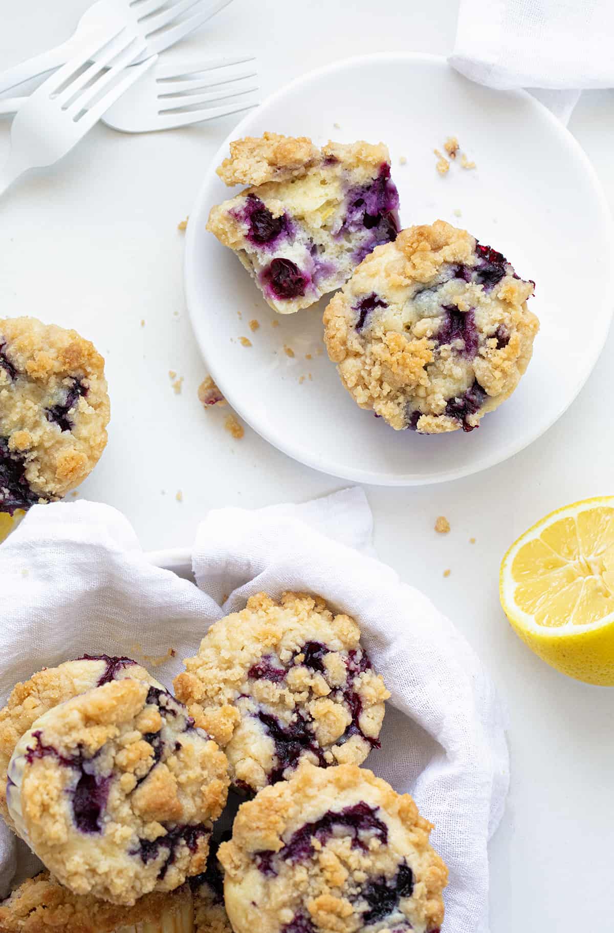 Blueberry Lemon Muffins in a Towel Lined Bowl Next to Muffins on a Plate with Fresh Lemons. 