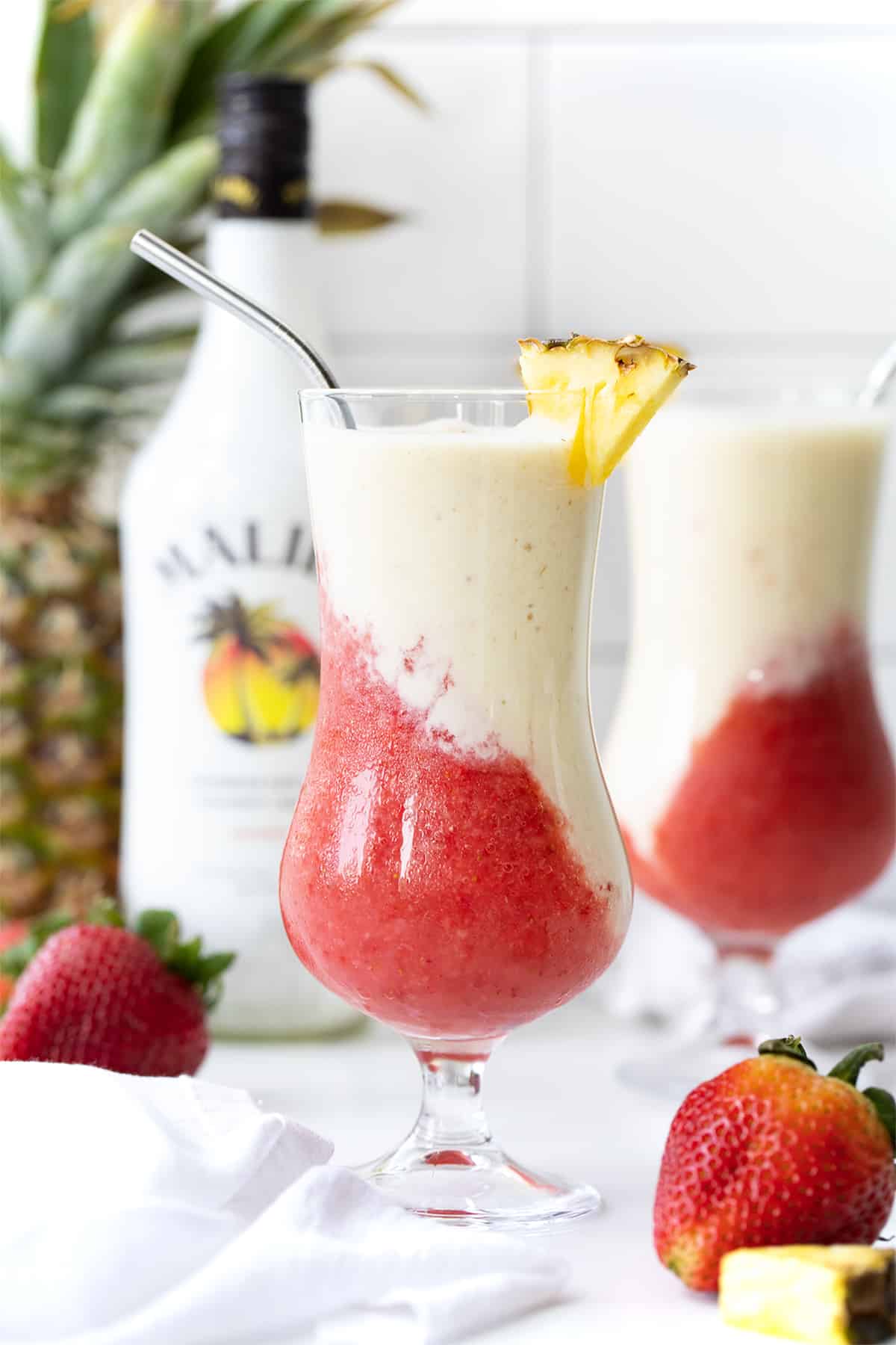 The Lava Flow Drink on a Counter with Pineapple, Malibu, and another Lava Flow Behind It.