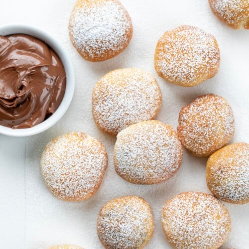 Nutella Bombs on a White Counter and Dusted with Confectioners Sugar Next to a Bowl of Nutella.