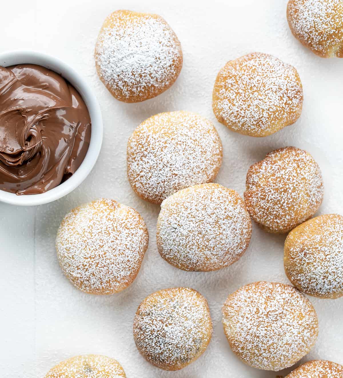 Nutella Bombs on a White Counter and Dusted with Confectioners Sugar Next to a Bowl of Nutella. 