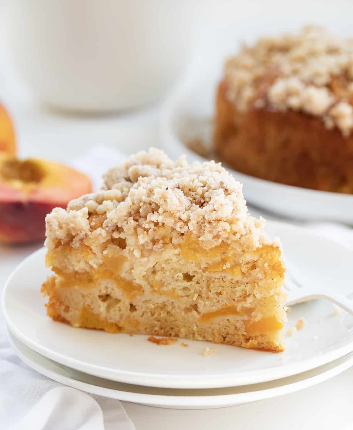 Peach Cake on a Plate with the Whole Cake Behind it and Peaches.