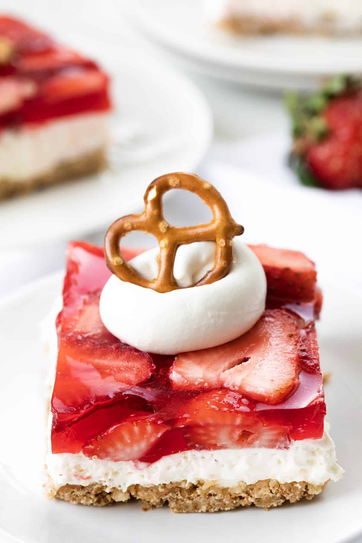 Strawberry Pretzel Salad on White Plates with Strawberries and a Pretzel on Top.