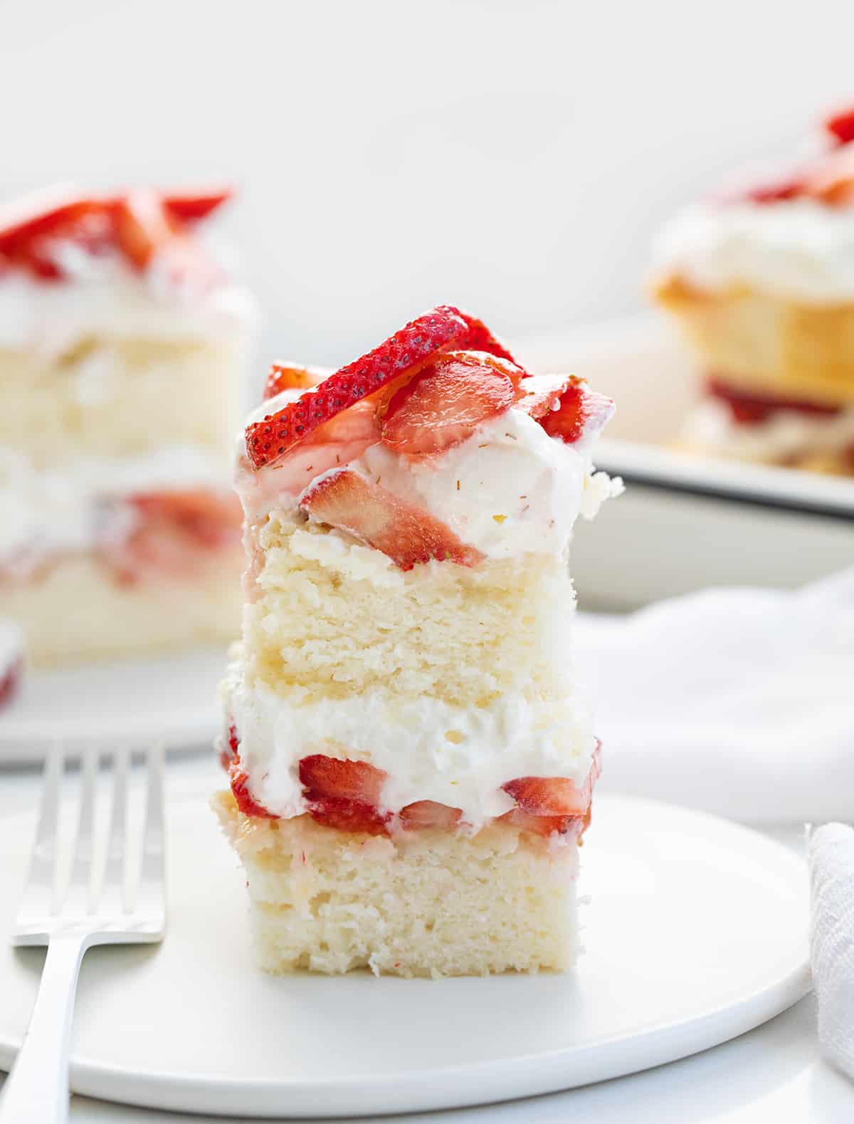 Slices of Sheet Pan Strawberry Shortcake on a White Counter with White Plates and Silverware.