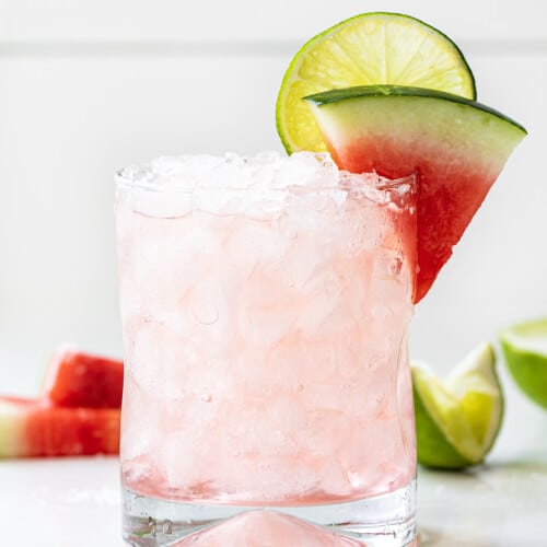 Glass Filled with a Watermelon Refresher Cocktail with a Watermelon Wedge and Lime.