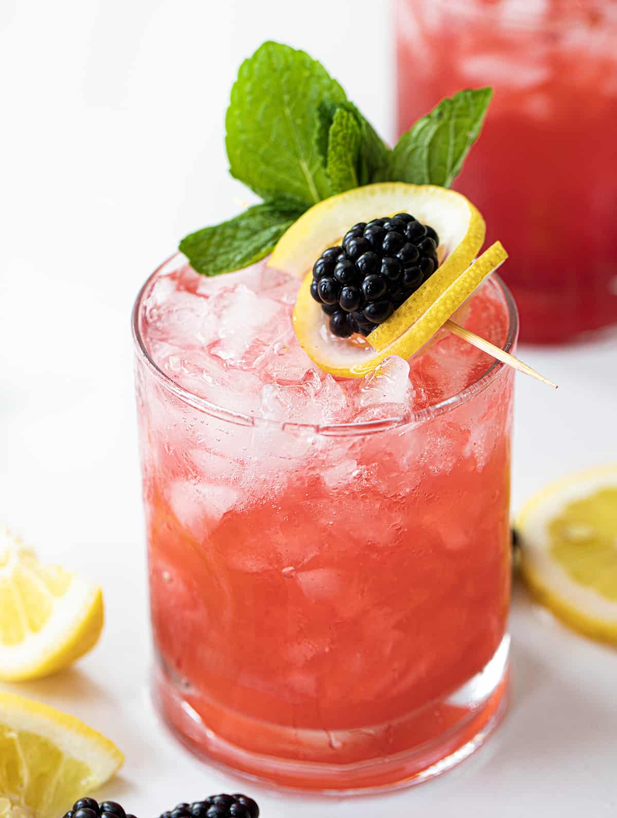 Blackberry Fizz Cocktails on a White Counter with Blackberry Lemon Garnish.