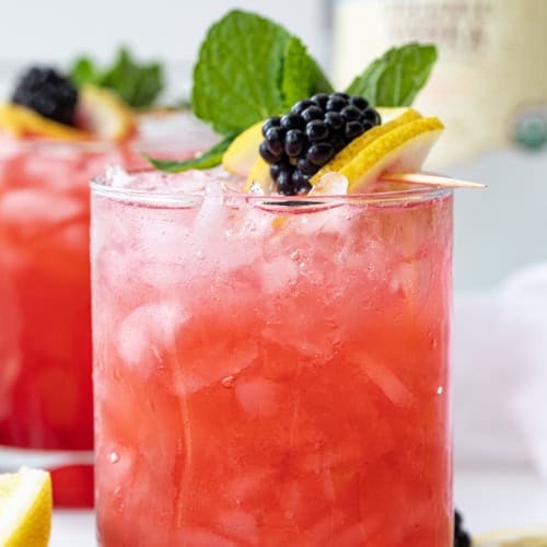 Blackberry Fizz Cocktails on a White Counter with Blackberry Lemon Garnish.