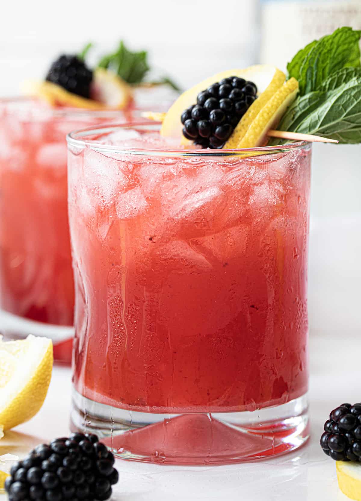 Blackberry Fizz Cocktails on a White Counter with Blackberry Lemon Garnish.  