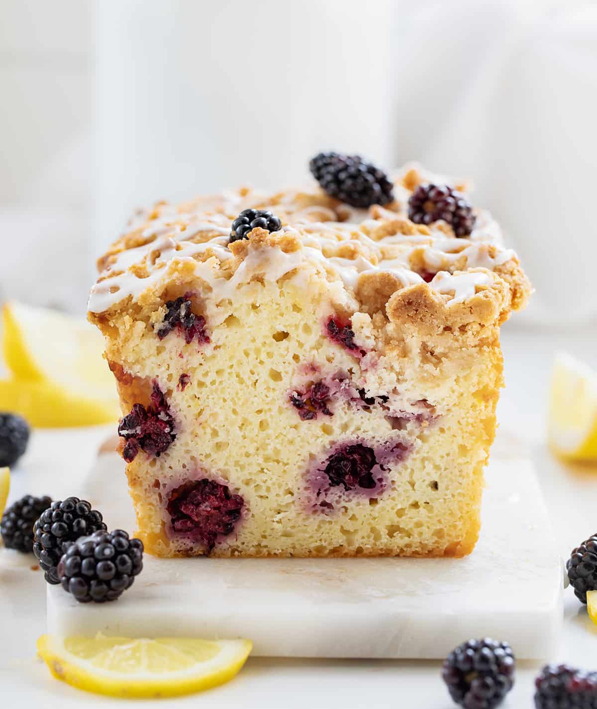 Blackberry Lemon Loaf on a Marble Cutting Board Surrounded by Blackberries and Lemon.